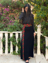 Woman wearing a black dress with red floral embroidery standing outdoors.